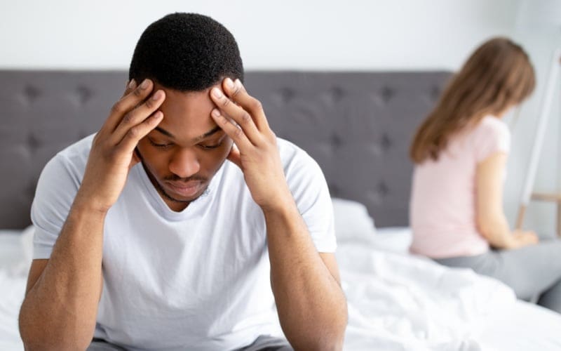 Erectile dysfunction, sex or relationship problems. Young black man sitting on bed, offended