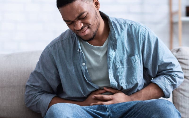 Man Having Painful Stomachache Touching Aching Stomach Sitting Indoors